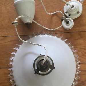 Op de afbeelding: Een vintage witte glazen plafondlamp met een decoratieve rand. De armatuur bevat een witte glazen kap, een katrolsysteem en een gedraaid snoer. De metalen accenten zijn messingkleurig. Het licht is ontworpen om aan het plafond te worden opgehangen.