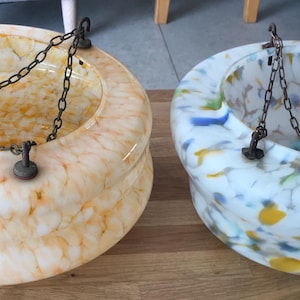 Puede incluir: Dos cuencos colgantes de vidrio con cadenas de metal. Un cuenco tiene un patrón veteado en tonos amarillos y blancos. El otro cuenco tiene un patrón veteado en azul, amarillo y blanco. Ambos cuencos son redondos con una amplia abertura.