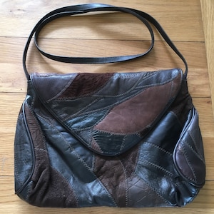 May include: A brown leather patchwork shoulder bag with a flap closure. The bag is made of different shades of brown leather and suede.