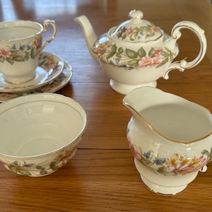 May include: A floral tea set comprising a teapot, creamer, sugar bowl, and teacup and saucer. The set features a white background with a delicate floral pattern in shades of pink, yellow, and green.