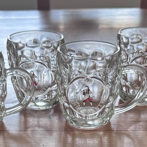May include: A set of six clear glass beer mugs featuring a dimpled exterior texture and a handle on the side. Each mug displays a circular logo with the text Whitbread Brewmaster and an illustration of a person wearing a kilt in the center.