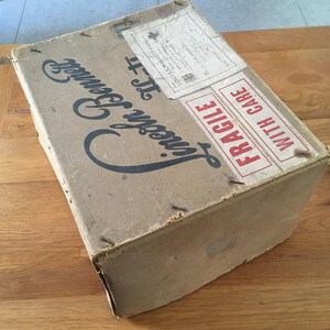 May include: A vintage cardboard box with the words "Lincoln Bennett" in a stylized font. The box has a shipping label and a "FRAGILE" sticker. The box is brown and appears aged.