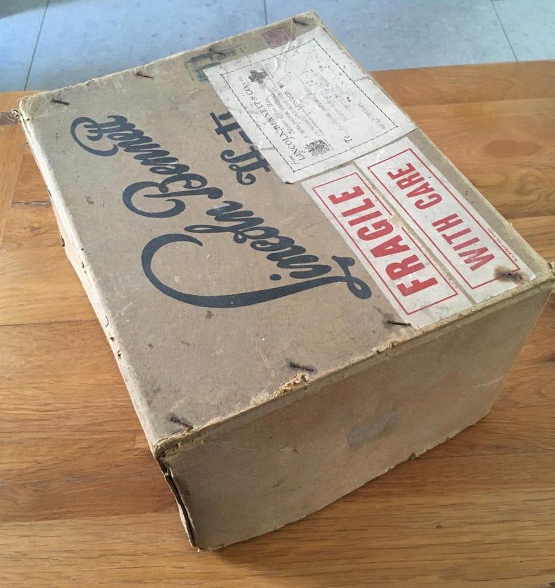 May include: A vintage cardboard box with the words "Lincoln Bennett" in a stylized font. The box has a shipping label and a "FRAGILE" sticker. The box is brown and appears aged.