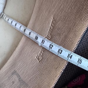 May include: Close-up of a beige fabric with a textured, ribbed pattern. A white measuring tape is laid across the fabric, showing measurements in inches. The fabric has a subtle sheen and a zipper is visible.
