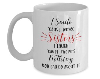 May include: White ceramic mug with a curved handle. The mug features the text "I Smile 'CAUSE WE'RE Sisters I LAUGH 'CAUSE THERE'S Nothing YOU CAN DO ABOUT IT" in black and red lettering.