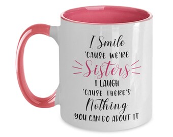 May include: White ceramic coffee mug with a pink interior and handle. The mug features a black and pink design with the text "I Smile 'cause we're Sisters I Laugh 'cause there's Nothing you can do about it."
