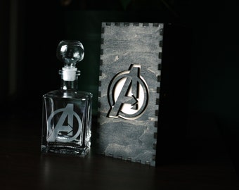 May include: A clear glass decanter with a stopper and a frosted Avengers logo. The decanter is in a wooden box with a cutout of the Avengers logo.