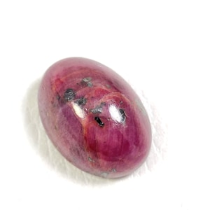 Op de afbeelding: Een ovale edelsteen met een glad, gepolijst oppervlak. De edelsteen is roze van kleur en heeft een paar donkere insluitsels.