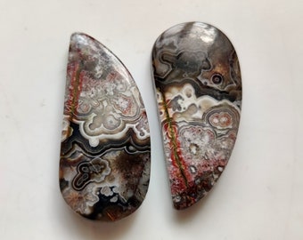May include: Two agate cabochons with a brown, white, and red pattern. The cabochons are shaped like a half-moon.