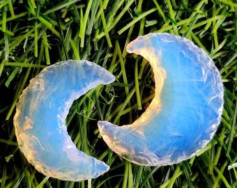 May include: Two blue and white crescent moon shaped pieces of opalite, a type of glass, on a green grass background.