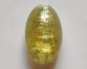 May include: A light green oval-shaped gemstone with red inclusions. The gemstone is smooth and polished.