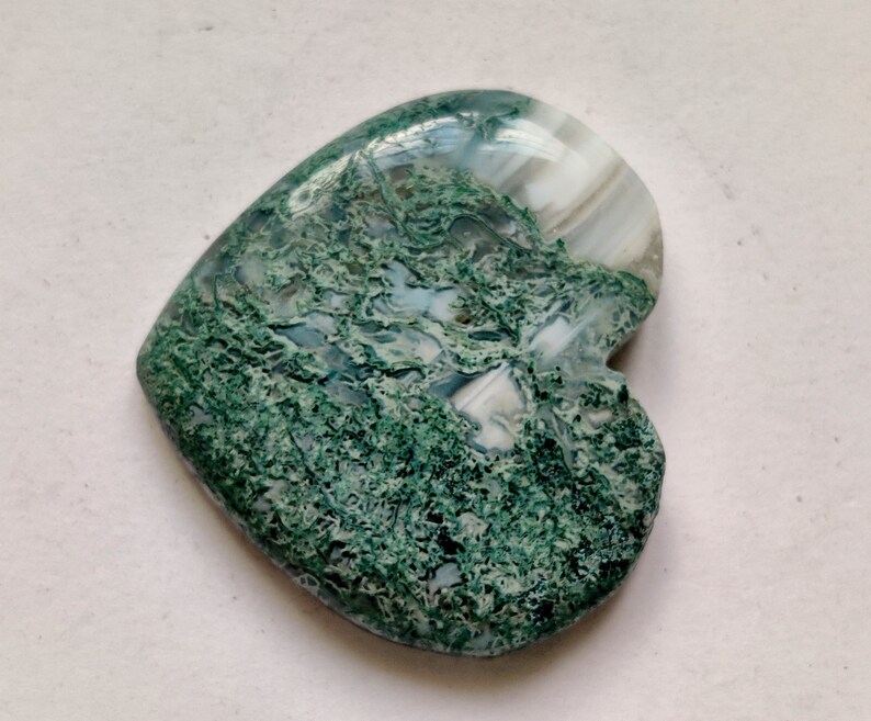 May include: A heart-shaped green and white agate cabochon with a swirling pattern. The stone is polished and has a smooth surface.