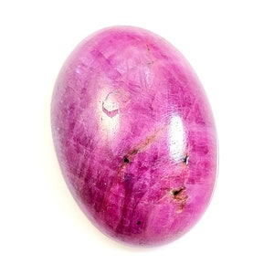 Puede incluir: Una gema pulida de forma ovalada en tonos rosa y magenta. La piedra tiene una superficie lisa con variaciones naturales de color y textura. La gema está sobre un fondo blanco.
