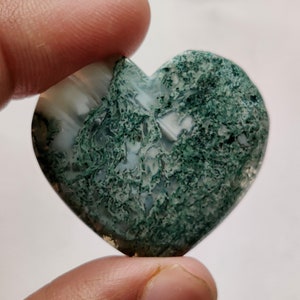 May include: A heart-shaped green moss agate with white and green patterns. The stone is polished and has a smooth surface.