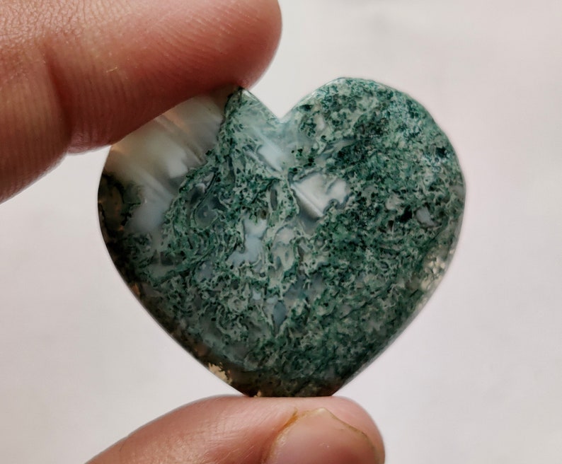 May include: A heart-shaped green moss agate with white and green patterns. The stone is polished and has a smooth surface.