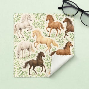 May include: A microfiber cleaning cloth featuring a repeating pattern of watercolor-style horses in various shades of brown, white, and tan. The horses are set against a backdrop of green foliage on a cream-colored background. Black eyeglasses are in the upper right corner.