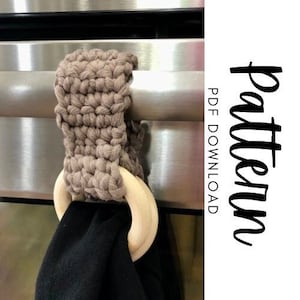 May include: A handmade, taupe-colored crochet towel holder with a wooden ring and a black towel. The holder is attached to a metal bar. The image includes the text "Pattern PDF Download".