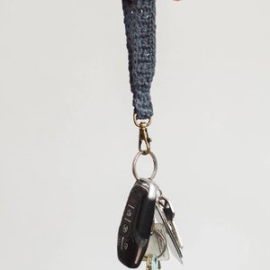 May include: A dark grey crocheted key chain with a silver key ring and a set of keys attached. The keys include a black car key fob and several silver house keys.
