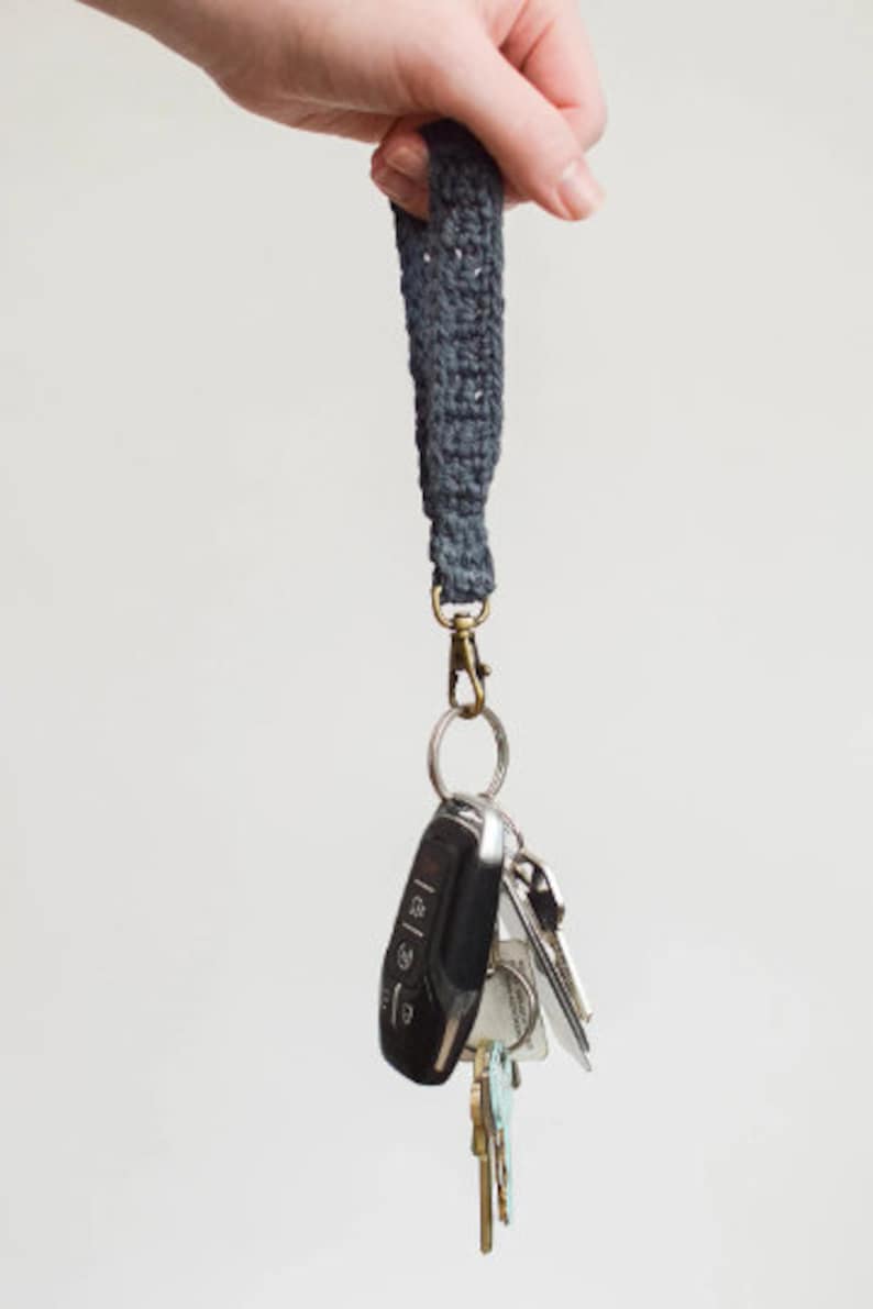 May include: A dark grey crocheted key chain with a silver key ring and a set of keys attached. The keys include a black car key fob and several silver house keys.