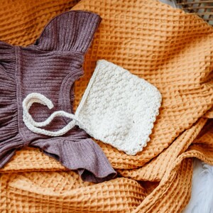 May include: A brown waffle knit blanket with a purple knitted dress and a white crocheted hat on top.