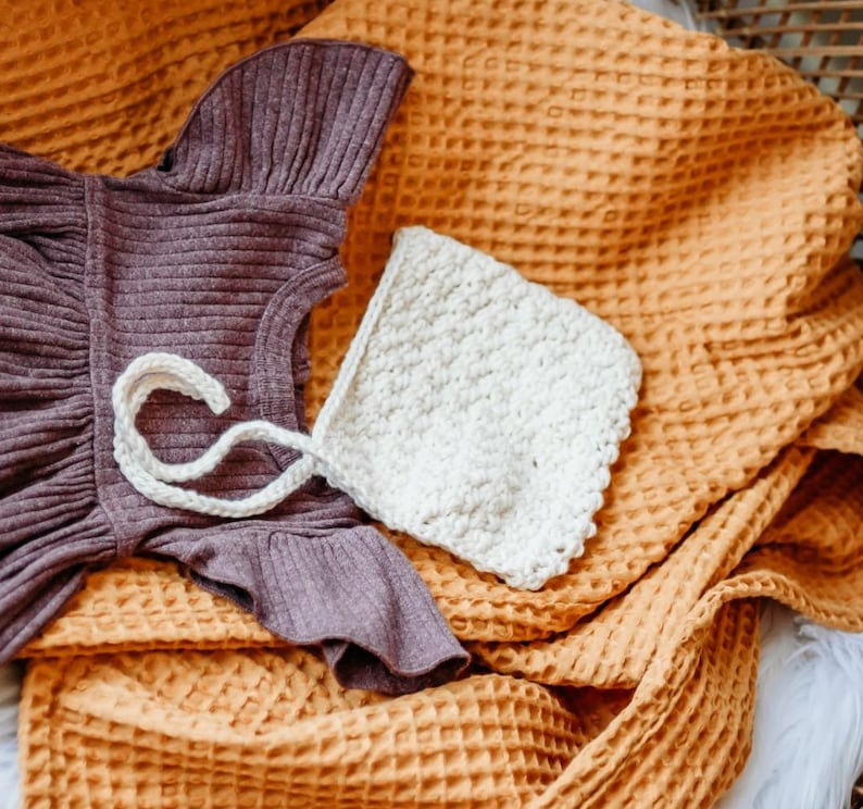May include: A brown waffle knit blanket with a purple knitted dress and a white crocheted hat on top.