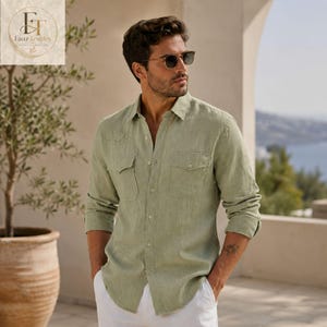 May include: A light sage green long-sleeve button-down shirt featuring two chest pockets with flaps, a classic collar, and a buttoned front placket. The shirt is worn with dark-tinted sunglasses and paired with white trousers.