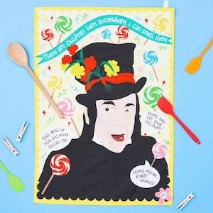 Peut inclure: Un torchon jaune avec une illustration fantaisiste d'un personnage portant un chapeau haut de forme noir avec des accents floraux. Le torchon comprend le texte "There are children here somewhere, I can smell them!" et des sucettes.