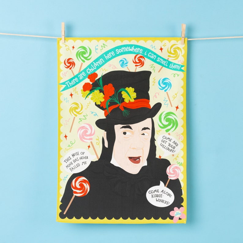 Może przedstawiać: Ż&oacute;łty ręcznik kuchenny z ilustracją postaci w czarnym kapeluszu z kwiatami. Dymki tekstowe zawierają frazy takie jak "Chodźcie po swoje lizaki!" i "Gdzieś tu są dzieci, czuję je!"