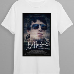 Op de afbeelding: Wit T-shirt met een zwart-witte afbeelding van Liam Gallagher van het album "Be Here Now". De afbeelding bevat de albumtitel en de tekst "Kicking up a storm since the day that he was born".