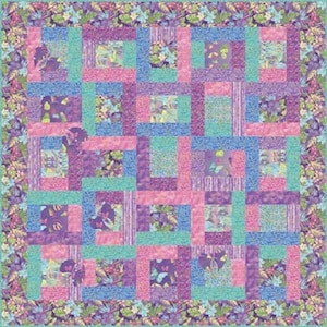 May include: A quilt with a patchwork design featuring squares of various shades of purple, pink, and blue. The squares are arranged in a grid pattern and feature a floral print. The quilt is bordered with a floral print fabric.