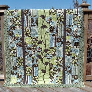 May include: A patchwork quilt with a brown, green and blue floral pattern. The quilt is hanging on a wooden railing.