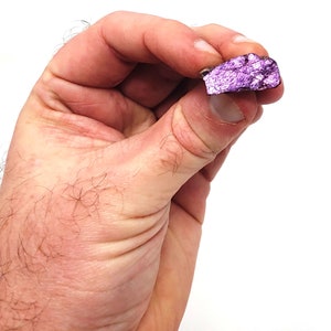 Pode incluir: Um close-up de uma amostra mineral de cor p&uacute;rpura e prateada. O mineral tem uma superf&iacute;cie &aacute;spera e irregular e um brilho met&aacute;lico.