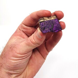 Pode incluir: Uma pedra bruta de forma irregular, com cores roxa e marrom.