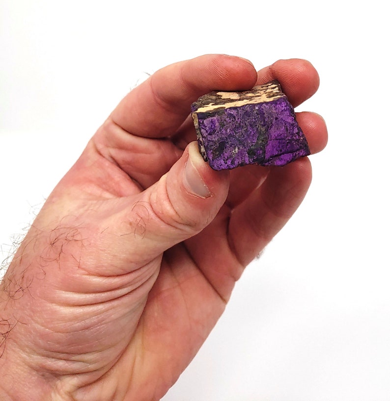 Pode incluir: Uma pedra bruta de forma irregular, com cores roxa e marrom.