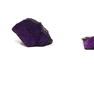 Pode incluir: Tr&ecirc;s esp&eacute;cimes minerais de cor p&uacute;rpura e preta de tamanhos diferentes, ao lado de uma moeda de 25 centavos de d&oacute;lar para a escala.