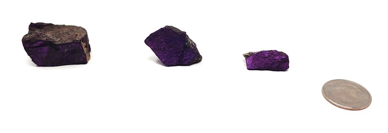 Pode incluir: Tr&ecirc;s esp&eacute;cimes minerais de cor p&uacute;rpura e preta de tamanhos diferentes, ao lado de uma moeda de 25 centavos de d&oacute;lar para a escala.