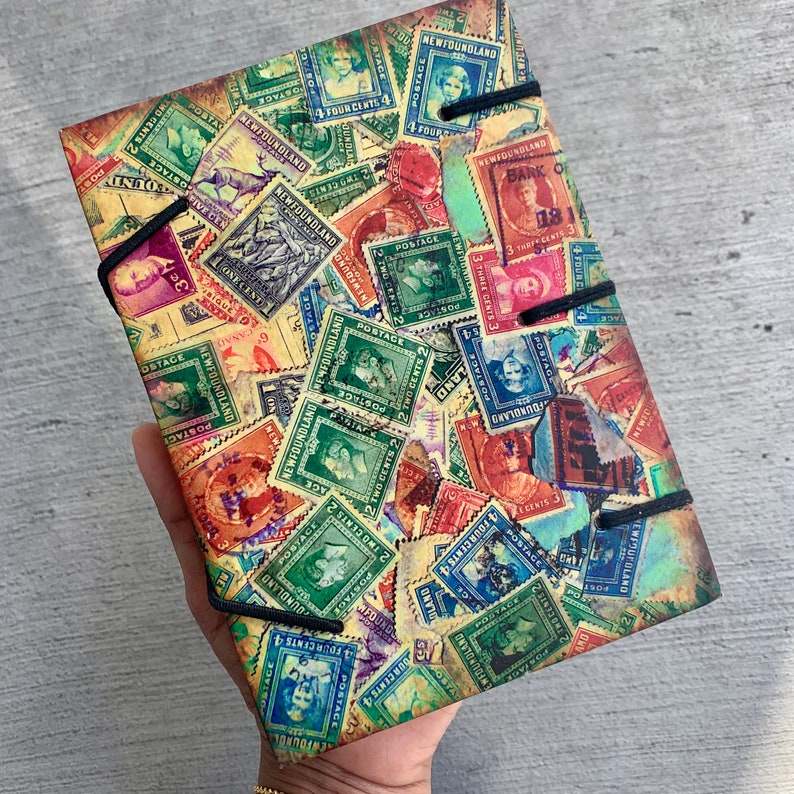 May include: A vintage-style notebook cover with a collage of colorful postage stamps featuring various designs and text, including "NEWFOUNDLAND" and "POSTAGE".