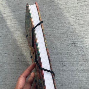 May include: A colorful, patterned notebook with a white spine and black string closure. The notebook has a wooden button closure.