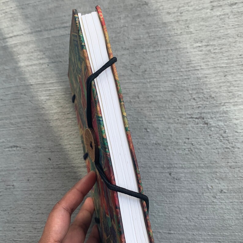 May include: A colorful, patterned notebook with a white spine and black string closure. The notebook has a wooden button closure.