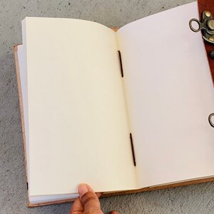 May include: A brown leather-bound journal with blank pages, open to reveal the cream-colored paper. The journal has a metal clasp and brown stitching.