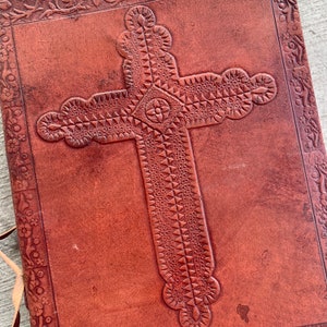 May include: A brown leather journal with a tooled cross design on the front cover.