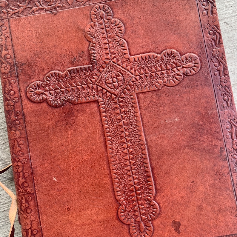 May include: A brown leather journal with a tooled cross design on the front cover.