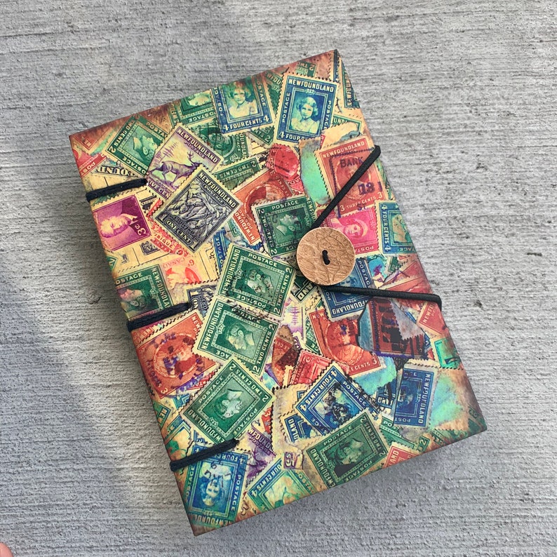 May include: A vintage-style journal cover with a collage of colorful postage stamps featuring images of people, animals, and landscapes. The cover is bound with a black cord and has a decorative button.