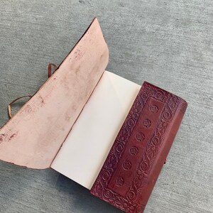 May include: A brown leather journal with an intricate floral design on the cover. The journal is open to reveal blank pages.