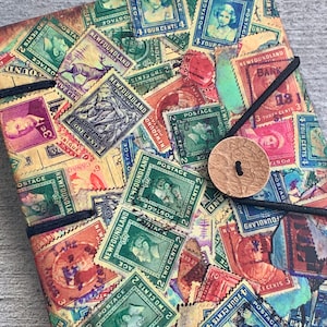 May include: A vintage-style notebook cover with a collage of colorful postage stamps featuring the text "Newfoundland" and various denominations. The stamps are arranged in a random pattern and have a faded, distressed look.