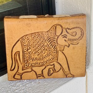 Könnte beinhalten: Ein braunes Lederjournal mit einem geprägten Elefantenmotiv auf dem vorderen Umschlag. Der Elefant ist in Braun umrandet und hat ein detailliertes Muster auf seinem Rücken.
