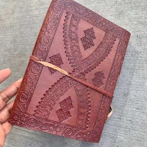 May include: A brown leather journal with intricate embossed floral and geometric patterns. The journal has a leather strap closure and is perfect for writing, journaling, or sketching.
