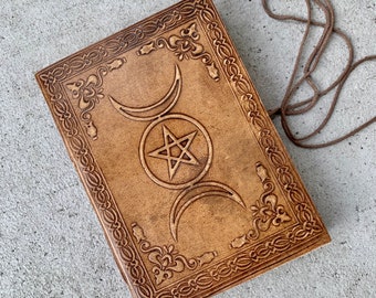 Könnte beinhalten: Ein braunes Lederjournal mit einem dreifachen Mond- und Pentagramm-Design. Das Journal hat einen dekorativen Rand und einen braunen Lederverschluss.