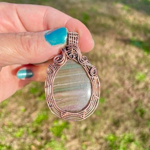 May include: A copper wire wrapped pendant featuring a green and white agate stone. The pendant is oval shaped and has a delicate wire design.