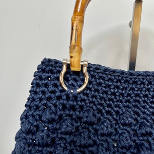 May include: A navy blue crocheted tote bag with a bamboo handle and silver hardware.